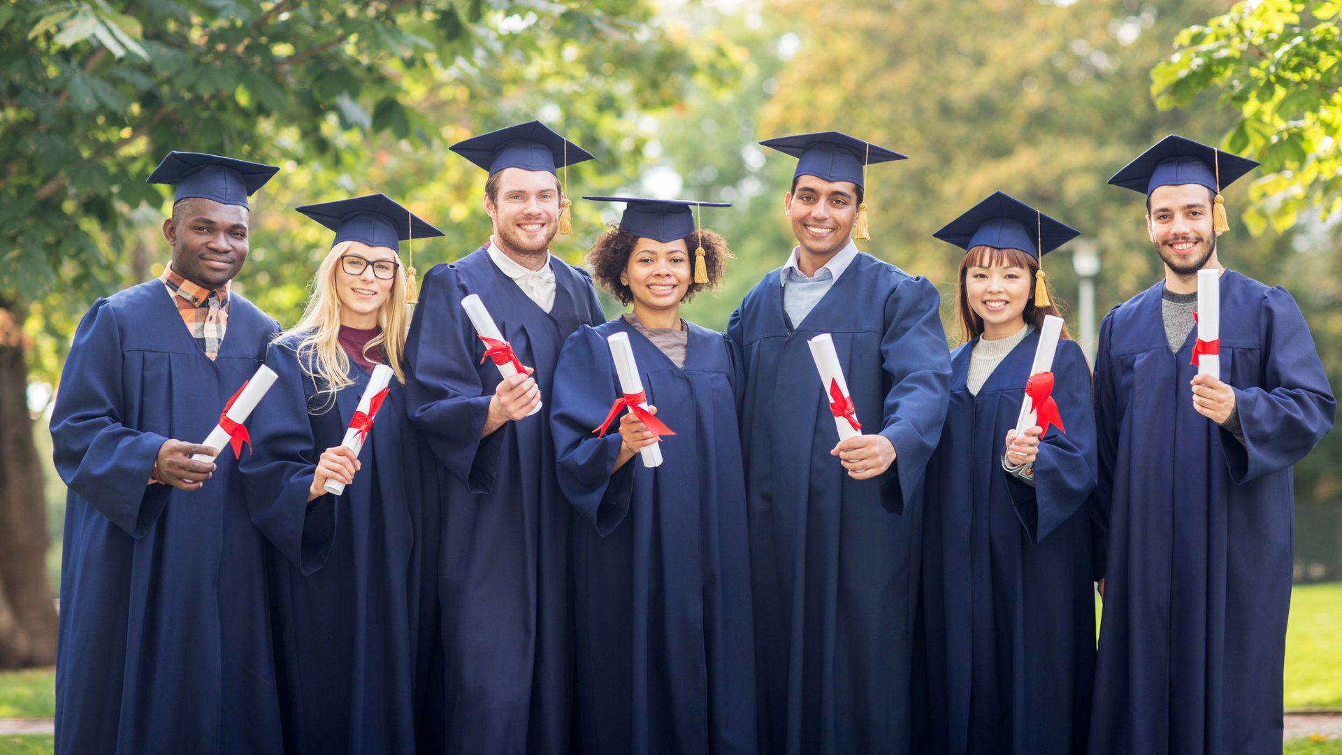 education, graduation and people concept - group of happy international students in mortar boards and bachelor gowns with diplomas